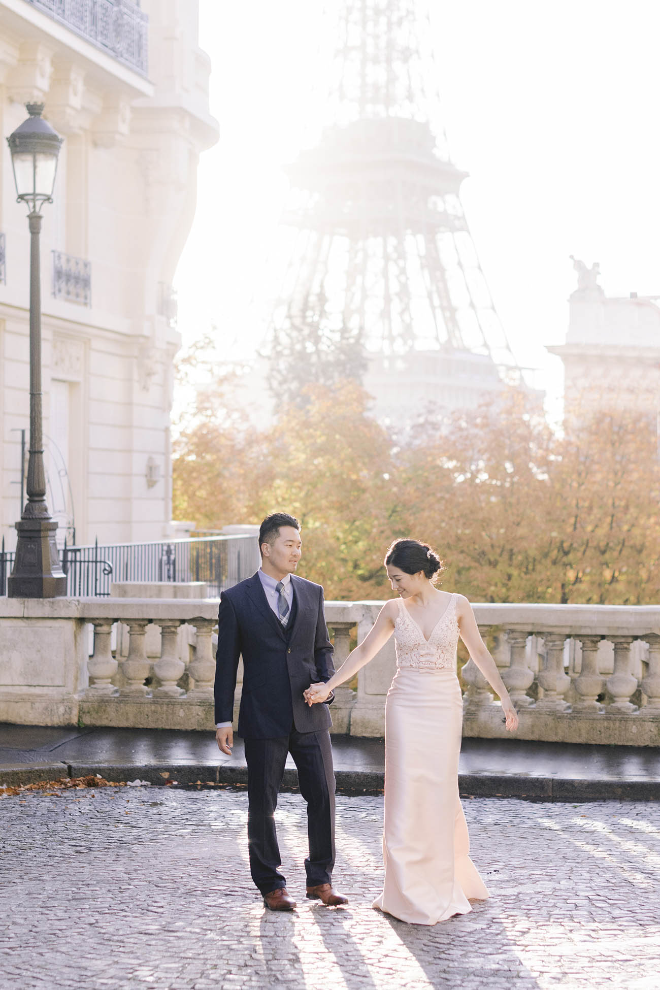  of the bride and groom walk on the street. Behind them the eiffel tower lit by morning light